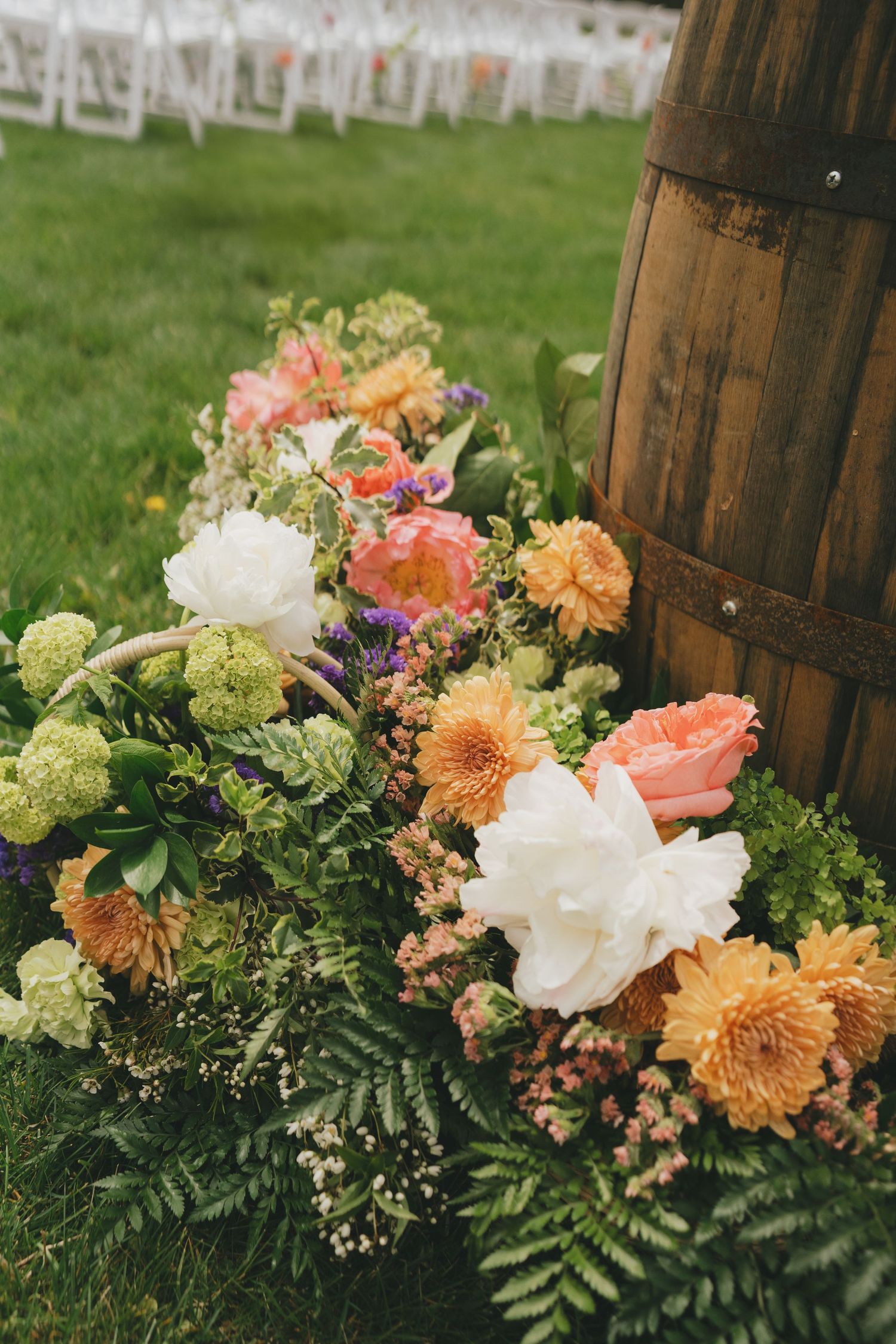 Lush floral arrangements in peach, white and coral colors displayed against rustic wooden barrels outdoors.
