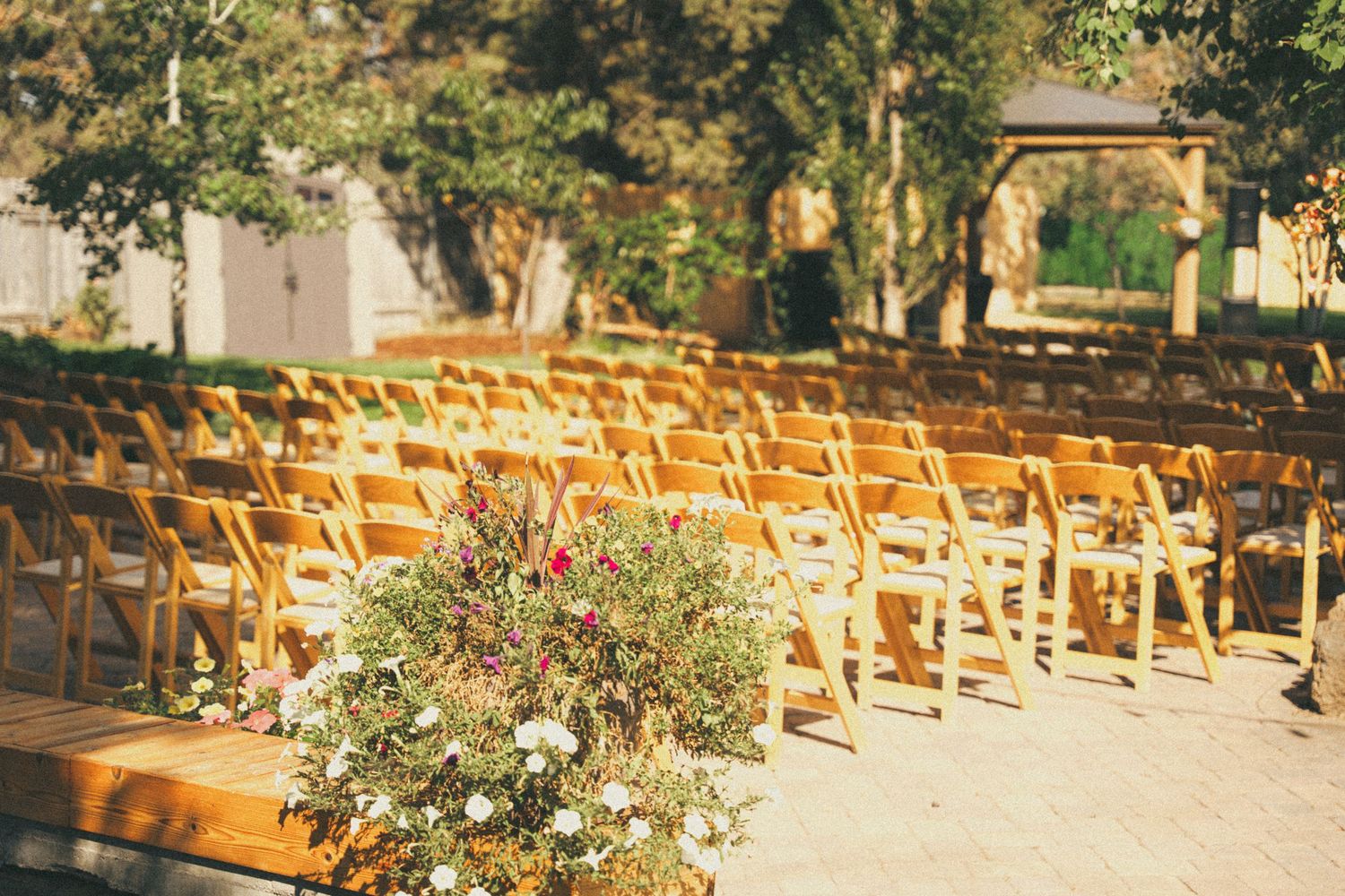 Rows of wooden folding chairs set up outdoors for a wedding ceremony, with a floral arrangement in the foreground.