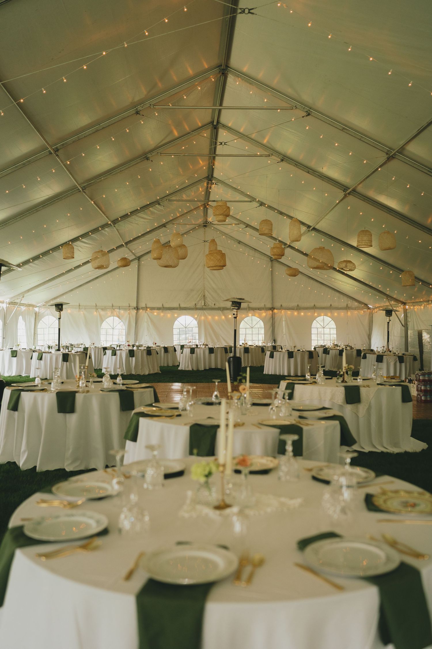 Wedding reception venue with white tent ceiling decorated with string lights and round dining tables set for guests.