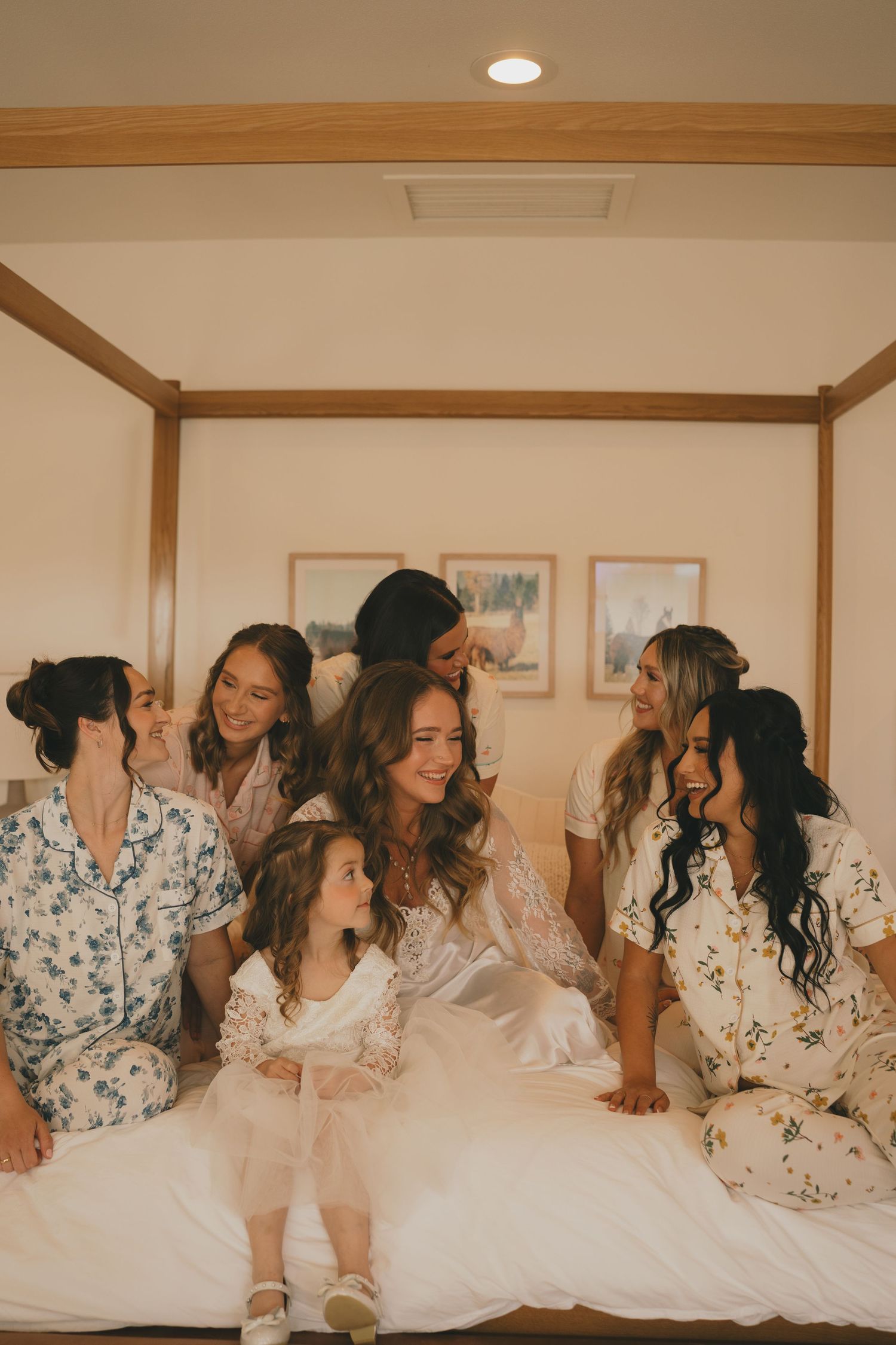 Group wearing matching floral robes gather on a bed in a warmly lit room.