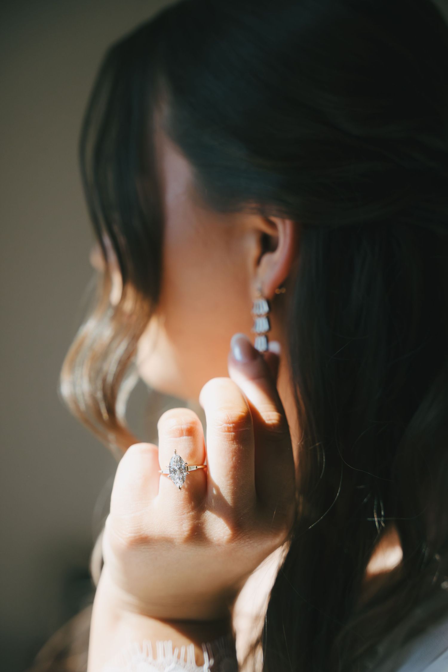 Close-up of a woman wearing a diamond engagement ring and elegant drop earrings in soft natural light.