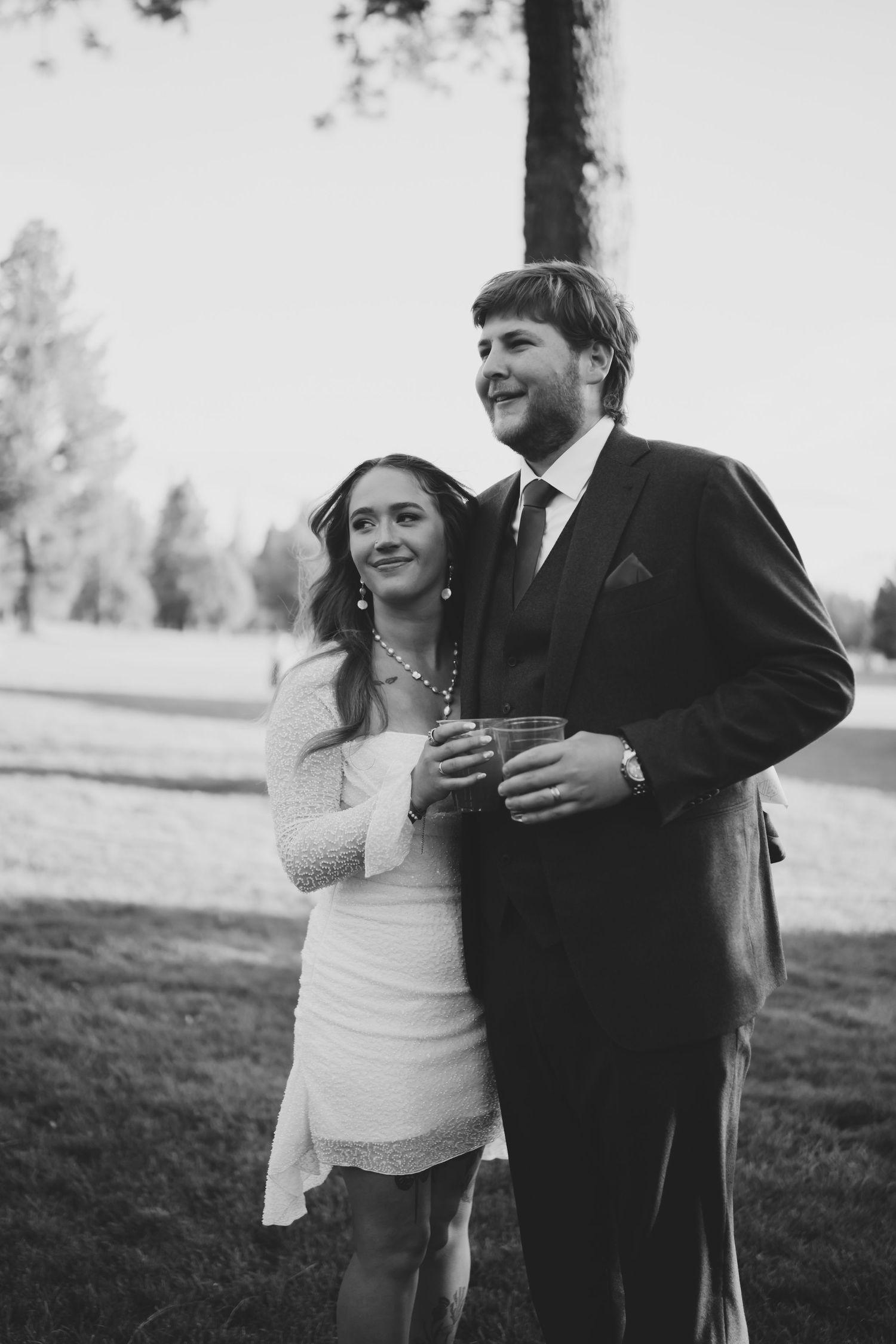 A couple shares a romantic moment outdoors in black and white, the bride in a fitted dress and groom in a dark suit.