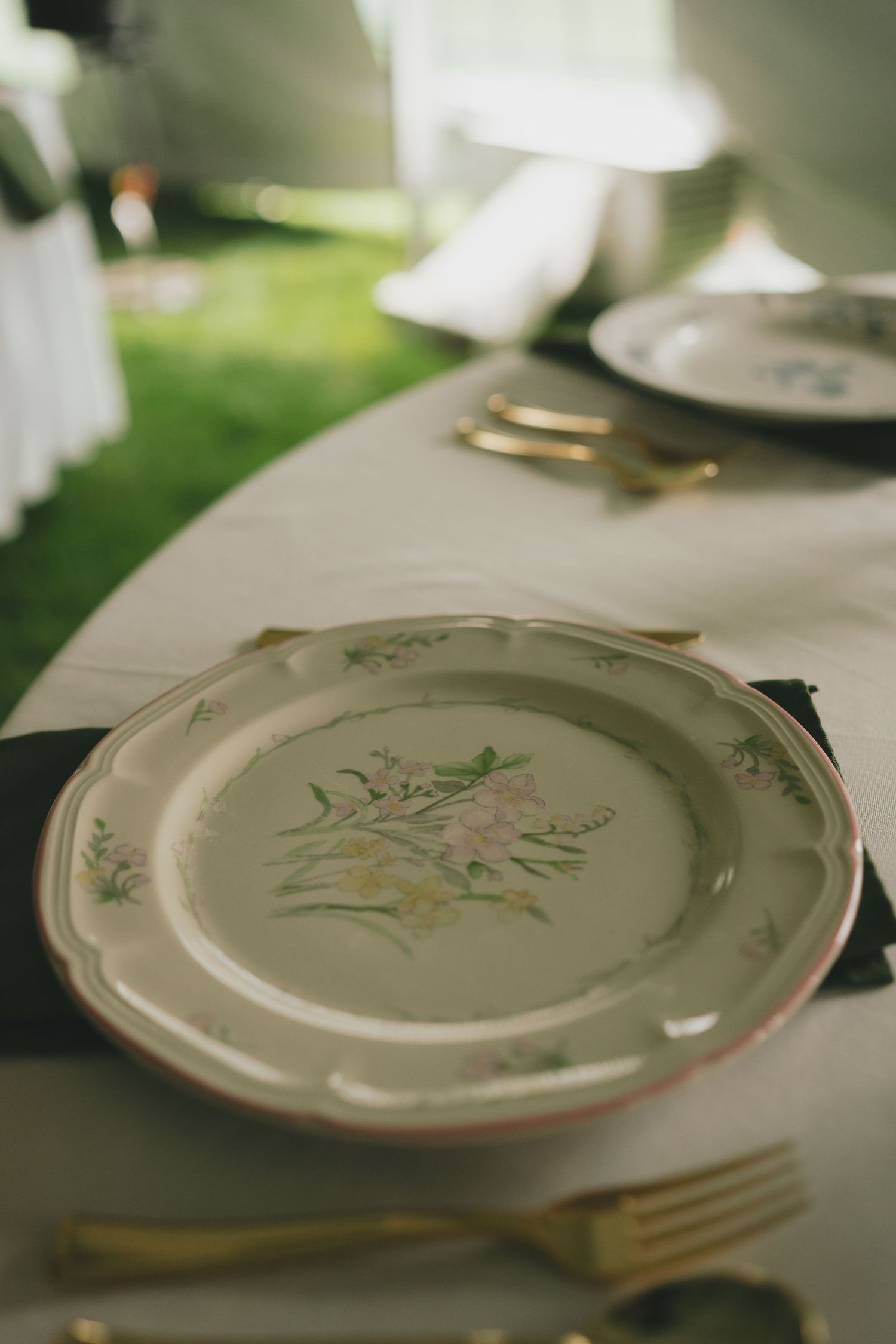 Vintage floral plate with delicate pink flower design and gold cutlery on a white tablecloth.