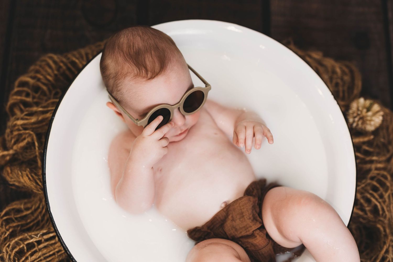Infant resting on white circular surface with brown plush toy.