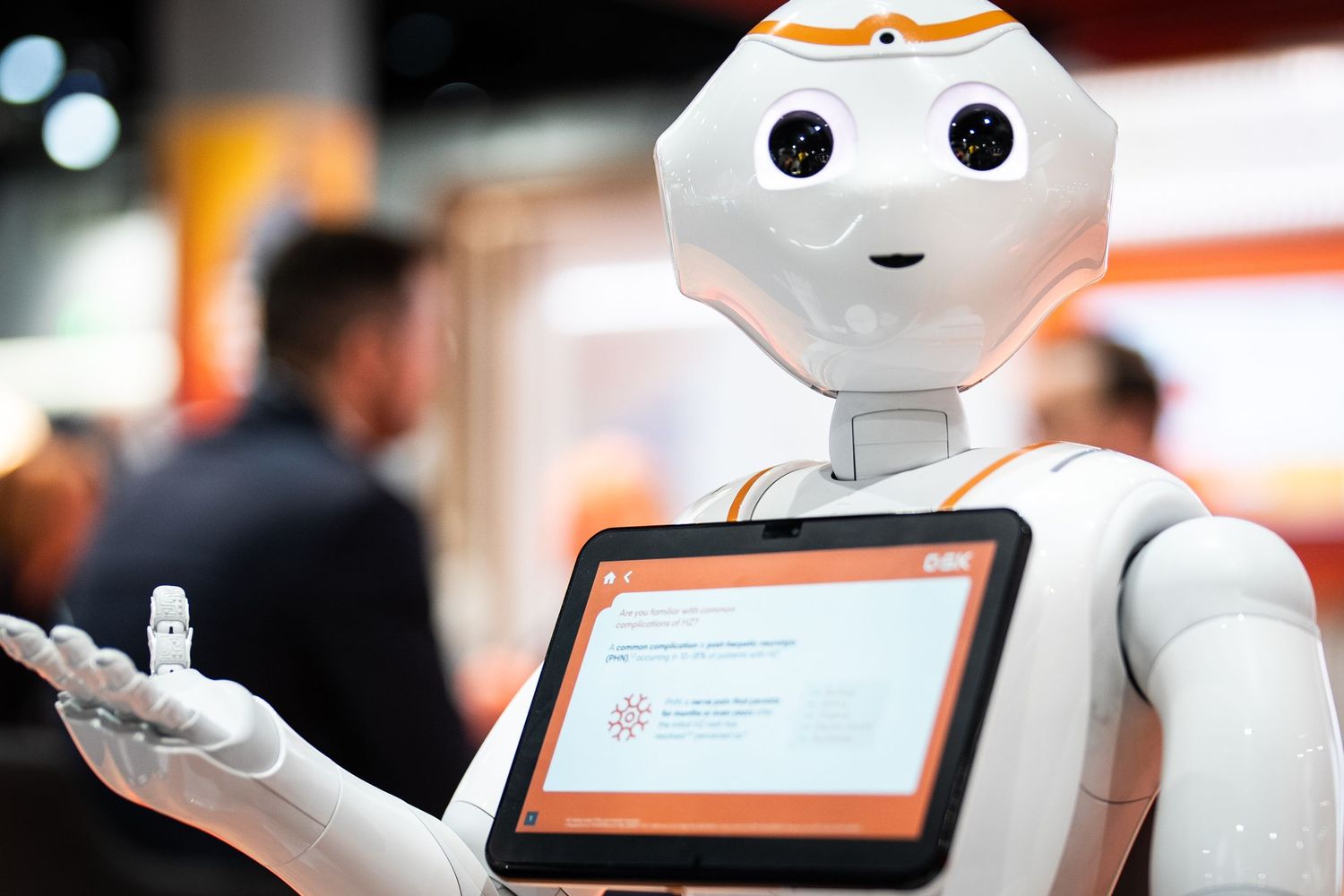 Pepper humanoid robot with tablet display gesturing at a tech exhibition event.