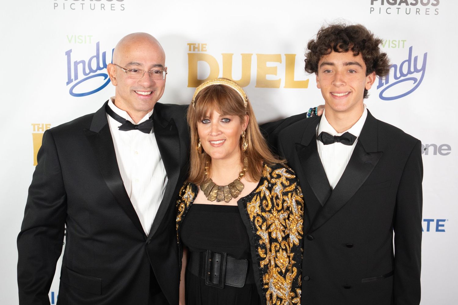 Three guests pose on red carpet at The Duel movie premiere, dressed in formal black attire.