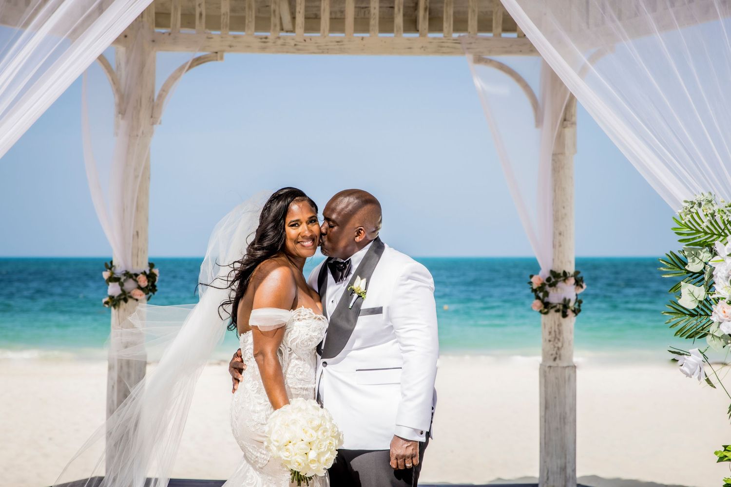Romantic beach wedding ceremony under white draped gazebos by turquoise waters.