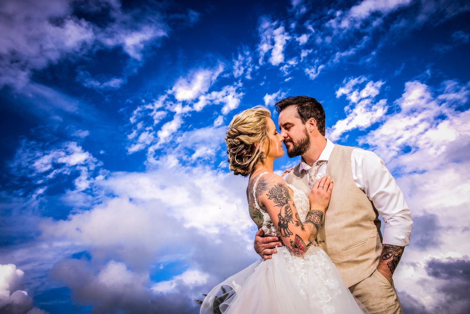 Wedding couple embracing under vibrant blue skies with dramatic clouds.