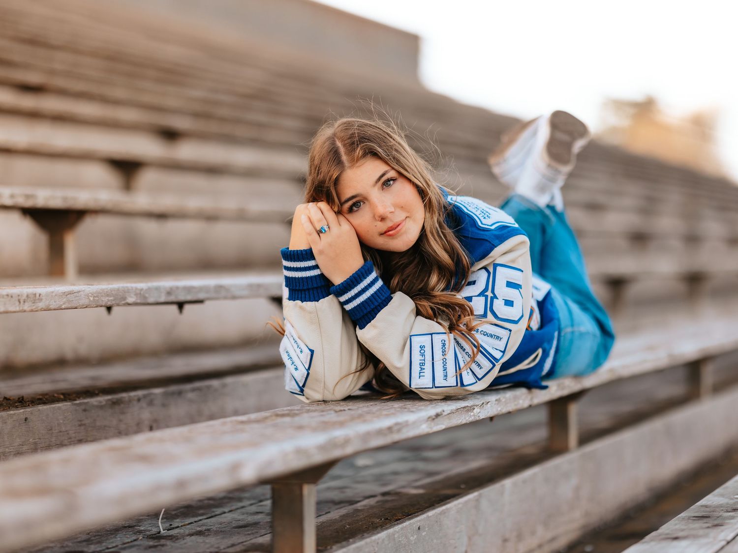 Young woman in cheerleader outfit lying on bleachers, posing thoughtfully with chin resting on hands.