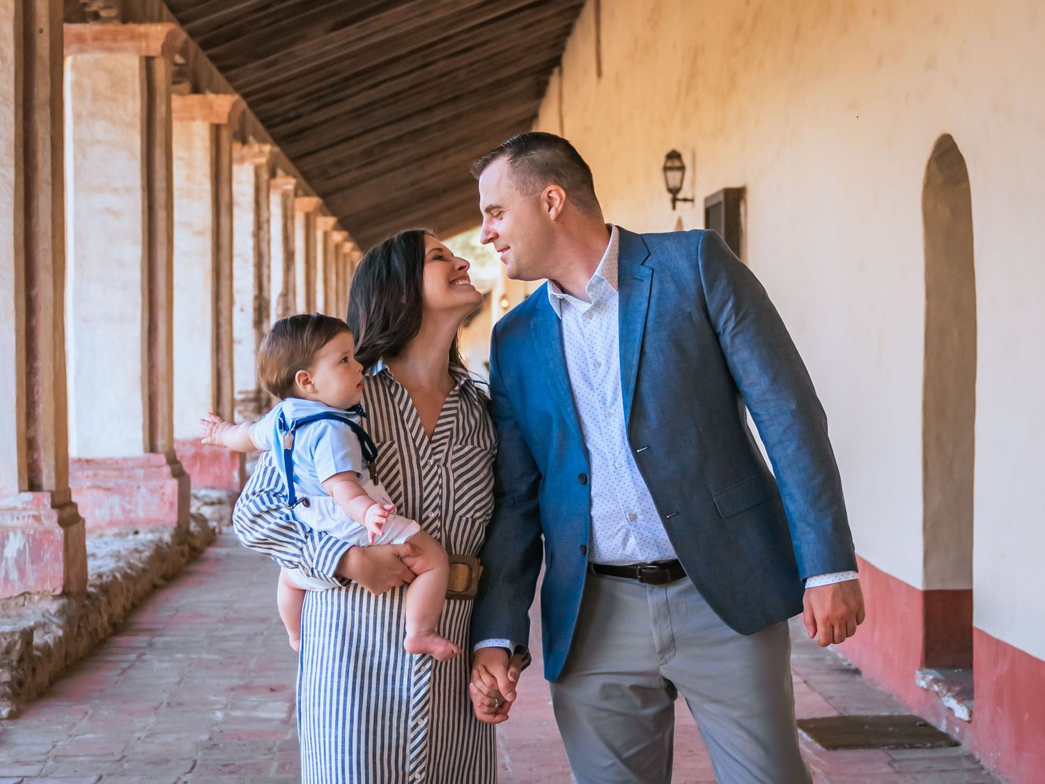 Family walks together along a covered outdoor hallway with arched columns and terra cotta walls in summer.