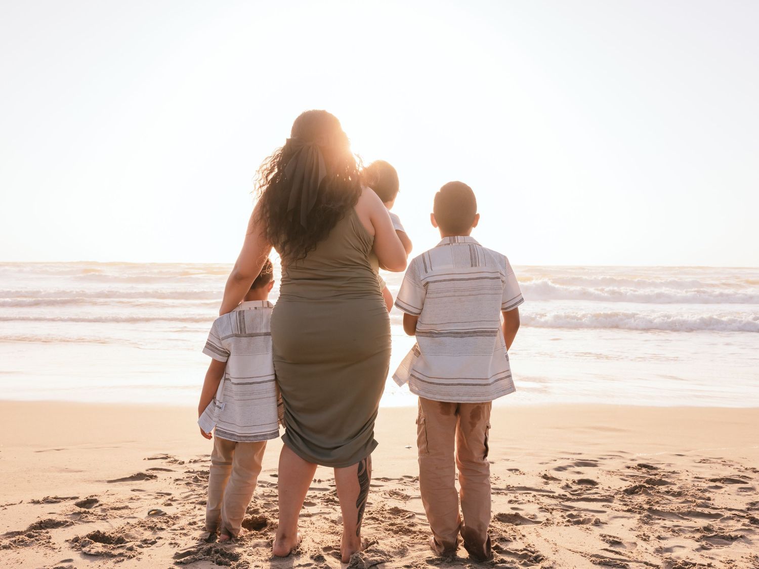 A family stands together on a sandy beach at sunset looking towards the ocean.