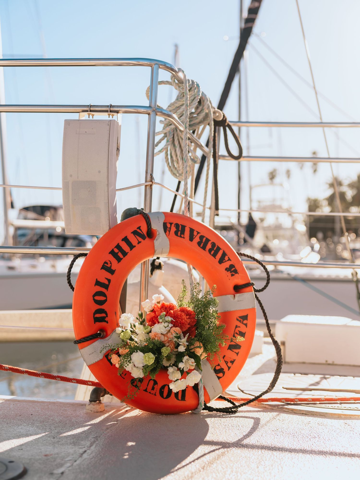 Orange life preserver ring with floral bouquet on sailboat deck at Santa Barbara Dolphin marina on sunny day.