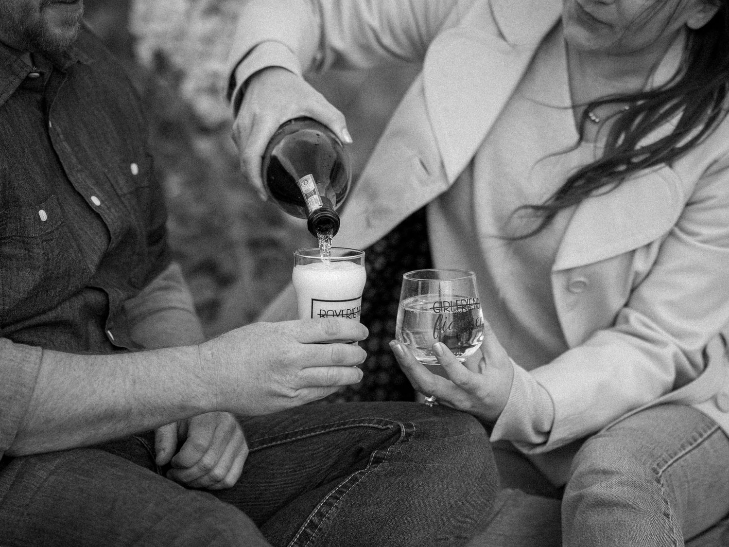 Black and white photo showing hands pouring wine into glasses during an outdoor gathering.