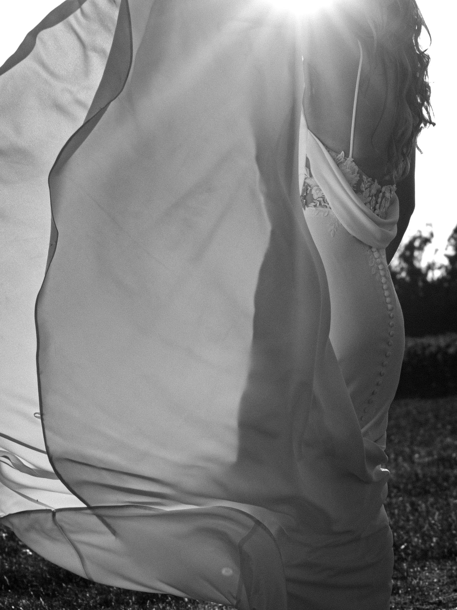 Black and white photo of a woman in a flowing white dress backlit by sunlight outdoors.