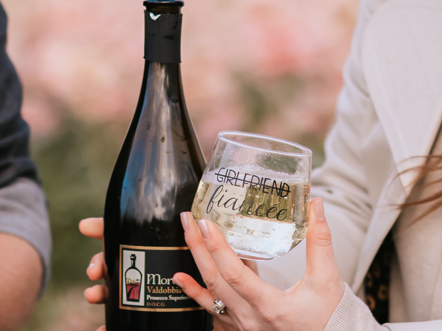 Two hands hold a dark wine bottle and stemless wine glass from Dollhead Winery during a tasting experience.