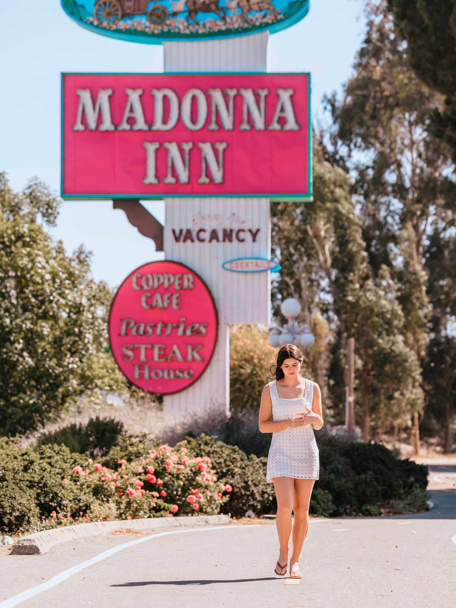 Woman in white dress walking in front of the iconic Madonna Inn sign in San Luis Obispo, California.