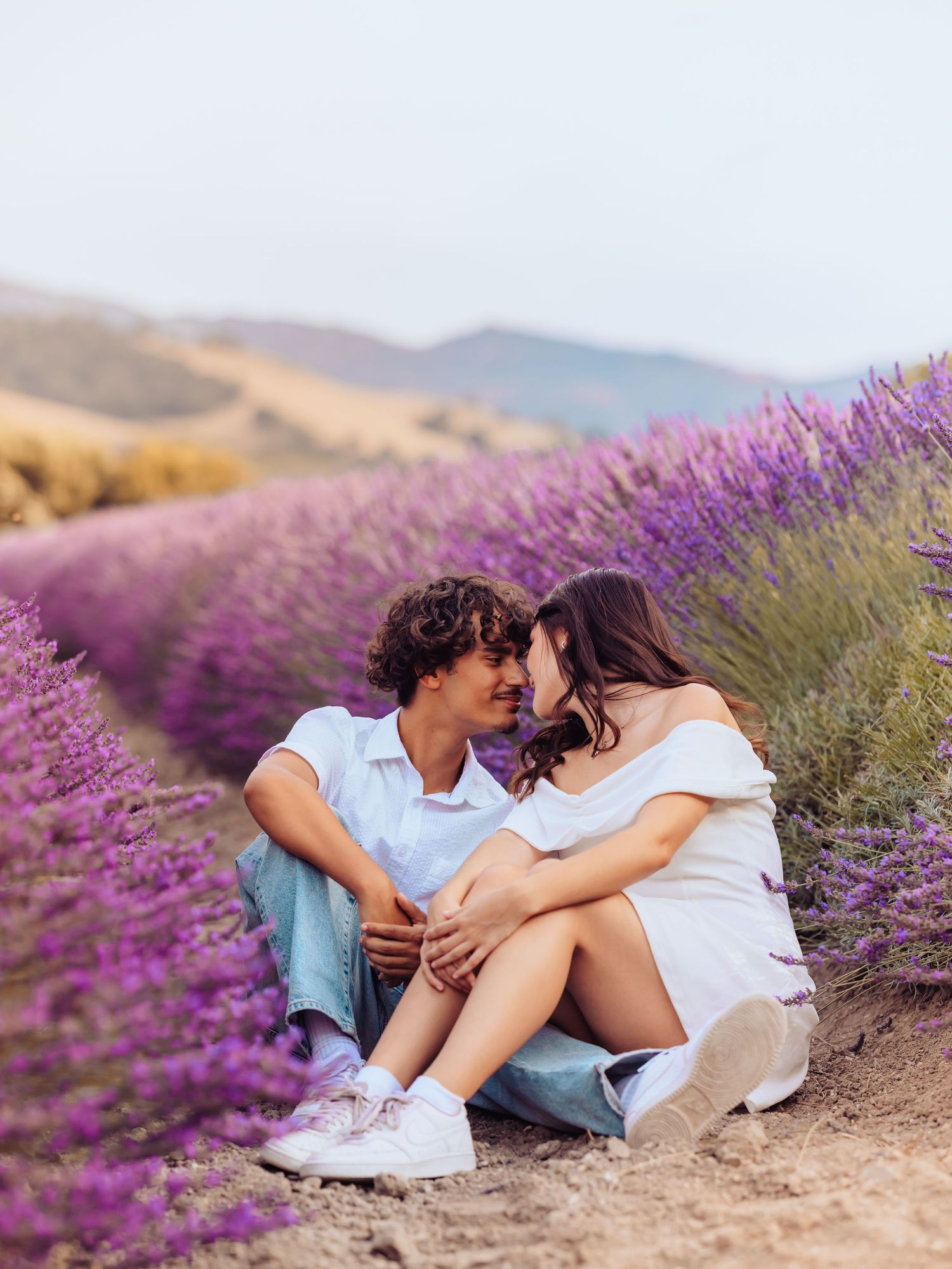 Couple sitting romantically in a blooming purple lavender field with rolling hills in the background.