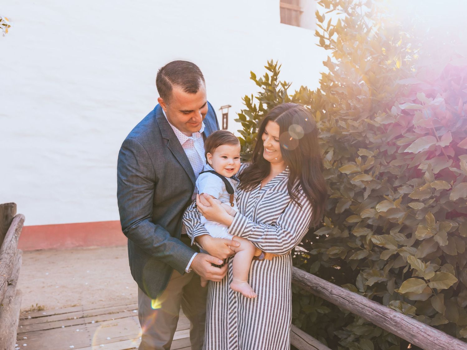 A couple in business casual attire stands together outdoors with a small child while enjoying a sunny afternoon.