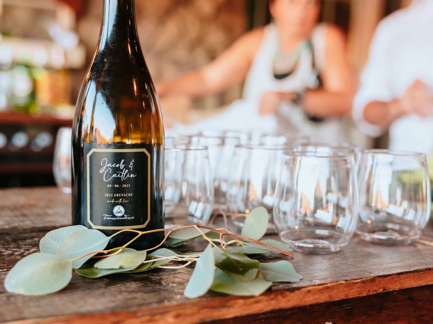 Wine bottle and empty glasses arranged on wooden surface with eucalyptus leaves for elegant table setting.