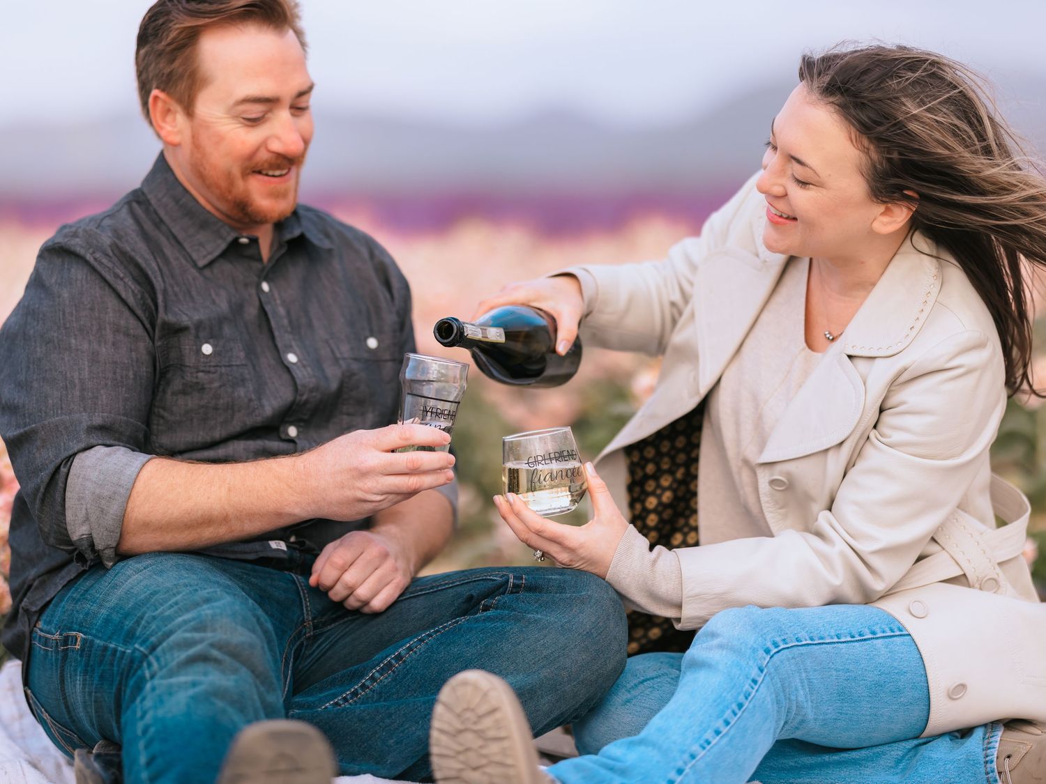 Two people having a picnic outdoors pouring wine and enjoying each other's company on a beautiful day.