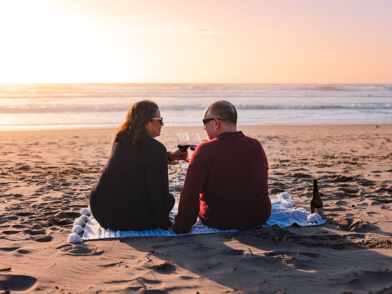 A couple sits together on a blanket watching the sunset over the beach at golden hour.