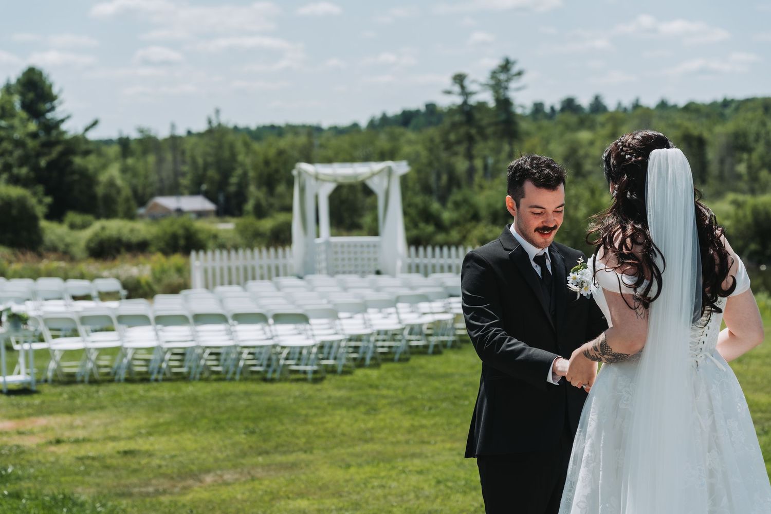 Groom shares a tender first look moment with his bride in a white veil at an outdoor wedding venue.