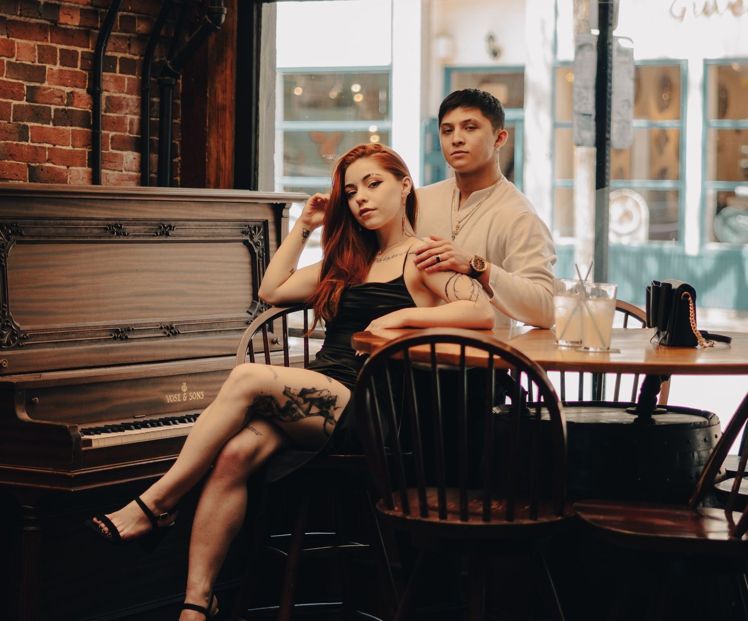A couple sits together in a cozy cafe near a vintage piano, the woman leaning back against the man.