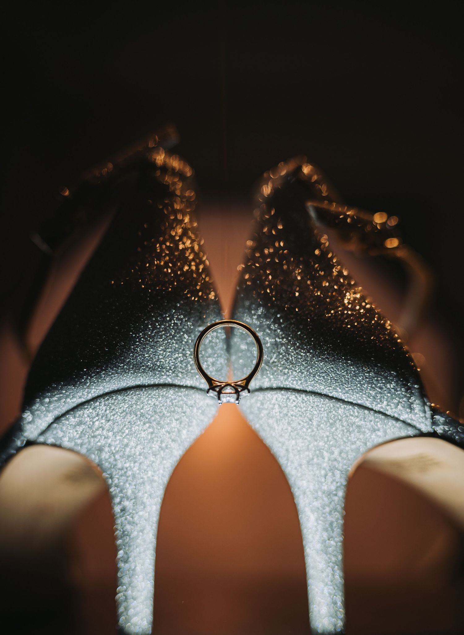 Close-up of a diamond engagement ring resting on glittering silver wedding heels.