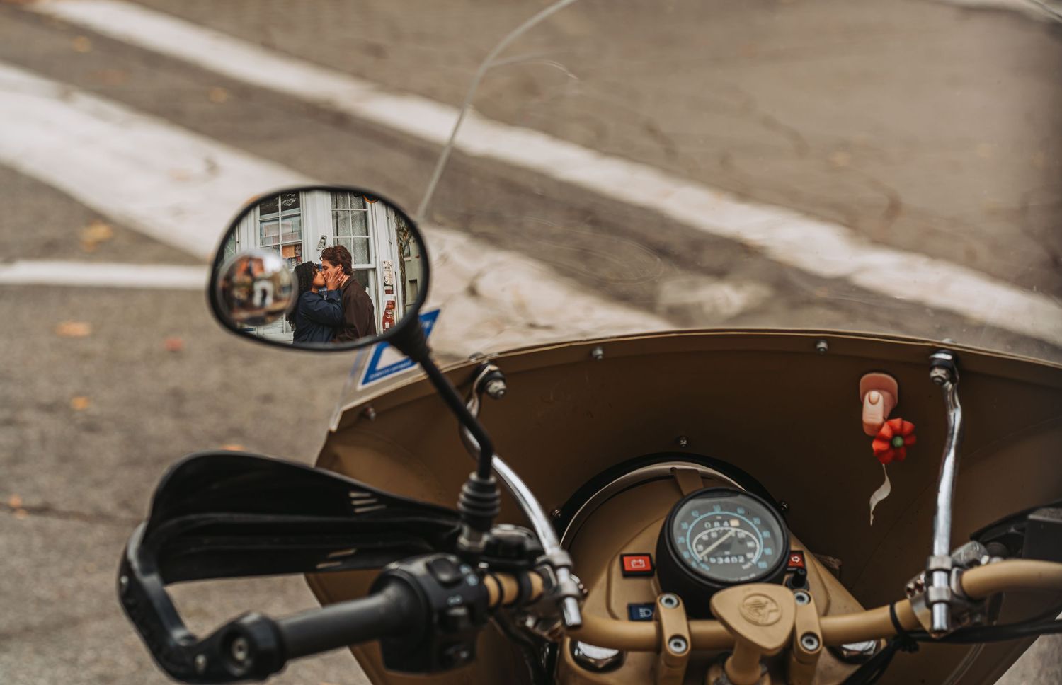 Close-up of a motorcycle cockpit with a rearview mirror reflecting a person, showcasing the speedometer and handlebars.