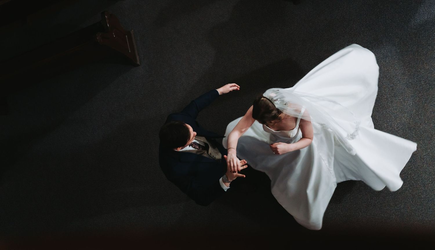 Aerial view of bride and groom dancing together on dark floor at wedding reception.