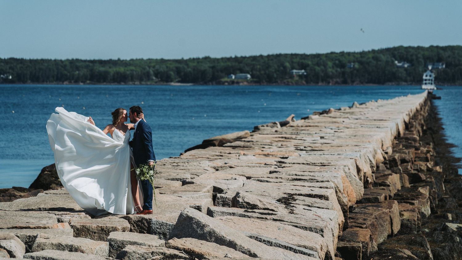 A bride and groom share a romantic moment on a rocky jetty by the ocean on their wedding day.