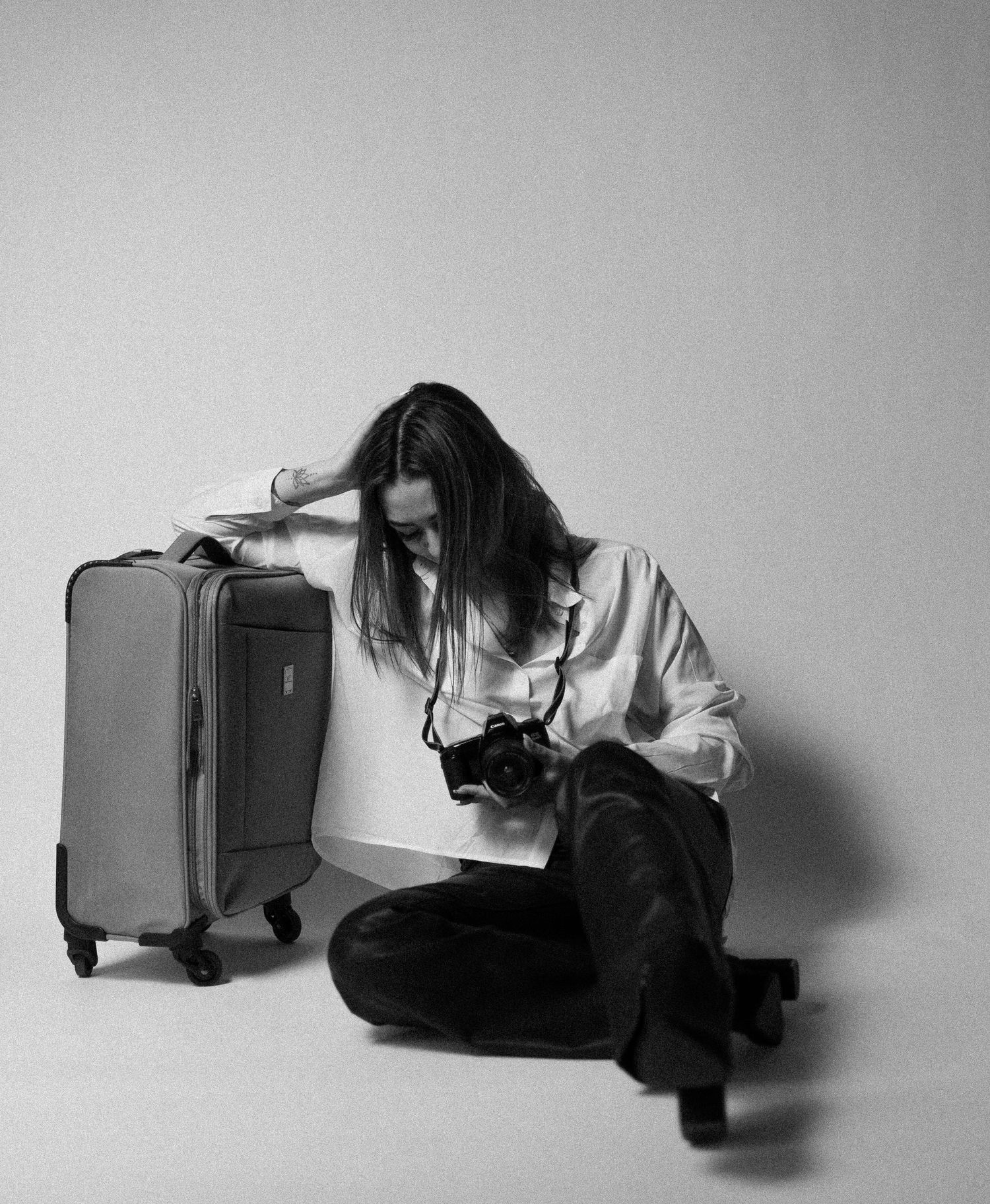 Black and white photo of woman sitting with luggage and camera on floor.