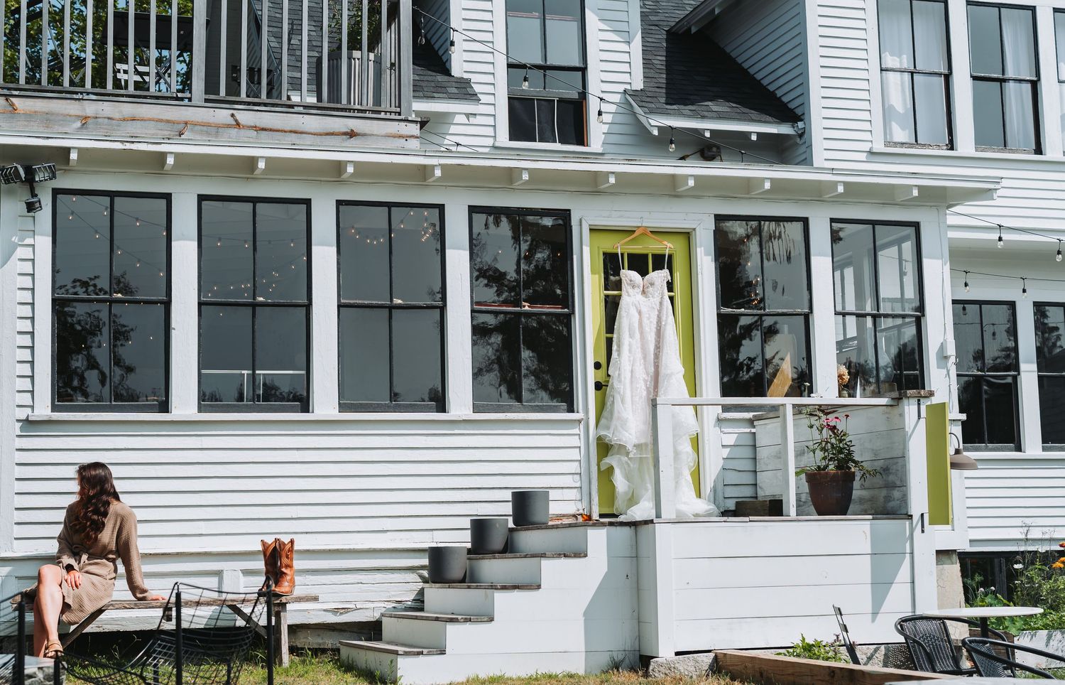 Woman relaxing outside a white clapboard house with yellow door on a sunny day.