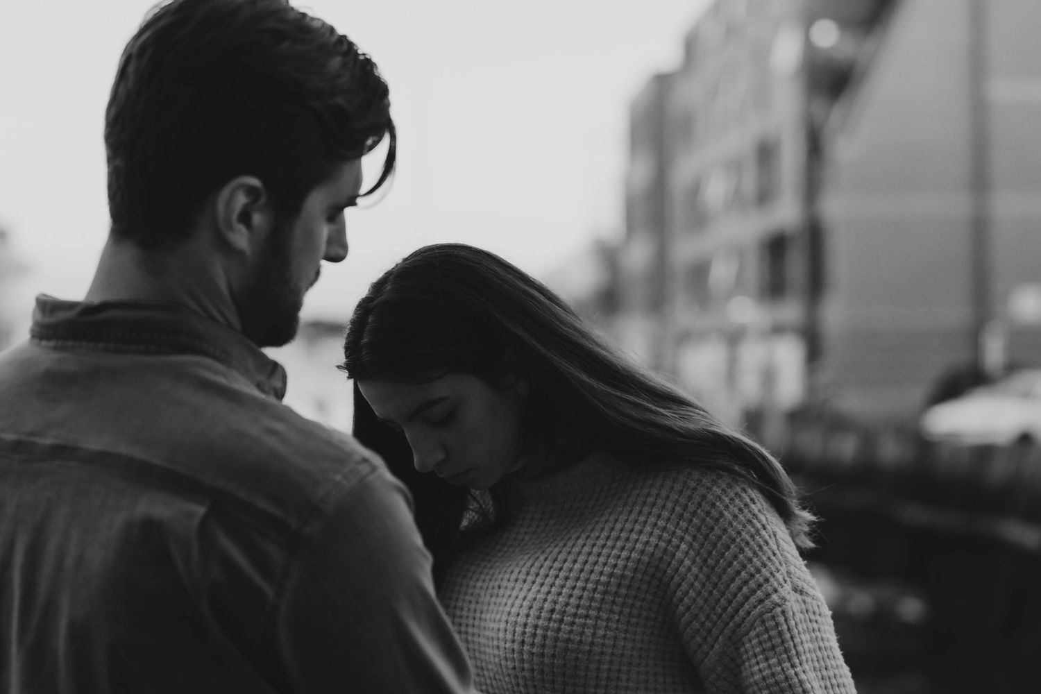 Black and white photo of a couple standing close together outdoors, woman looking down in a tender moment.