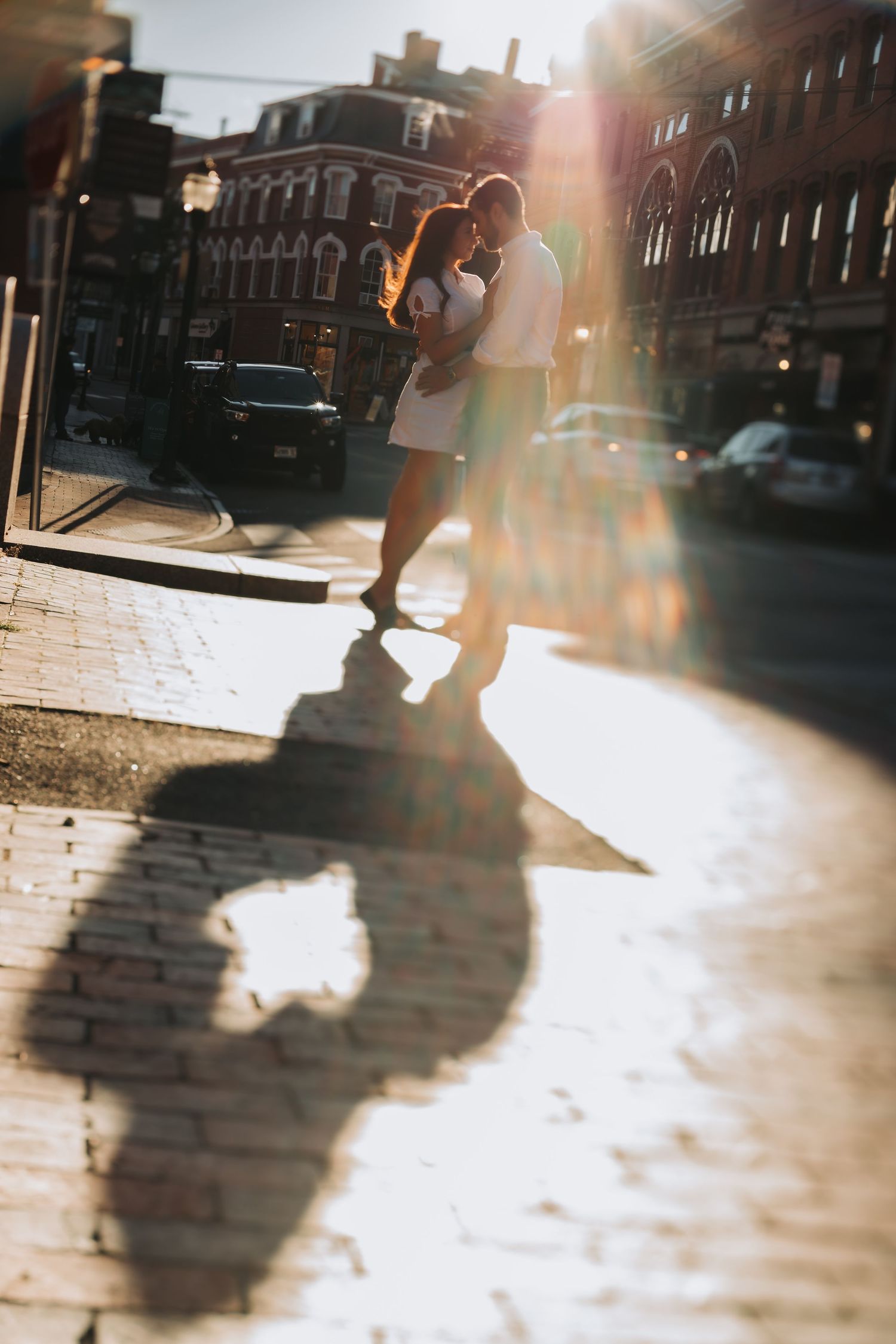 Couple embracing on sunlit cobblestone street with golden lens flare effect.