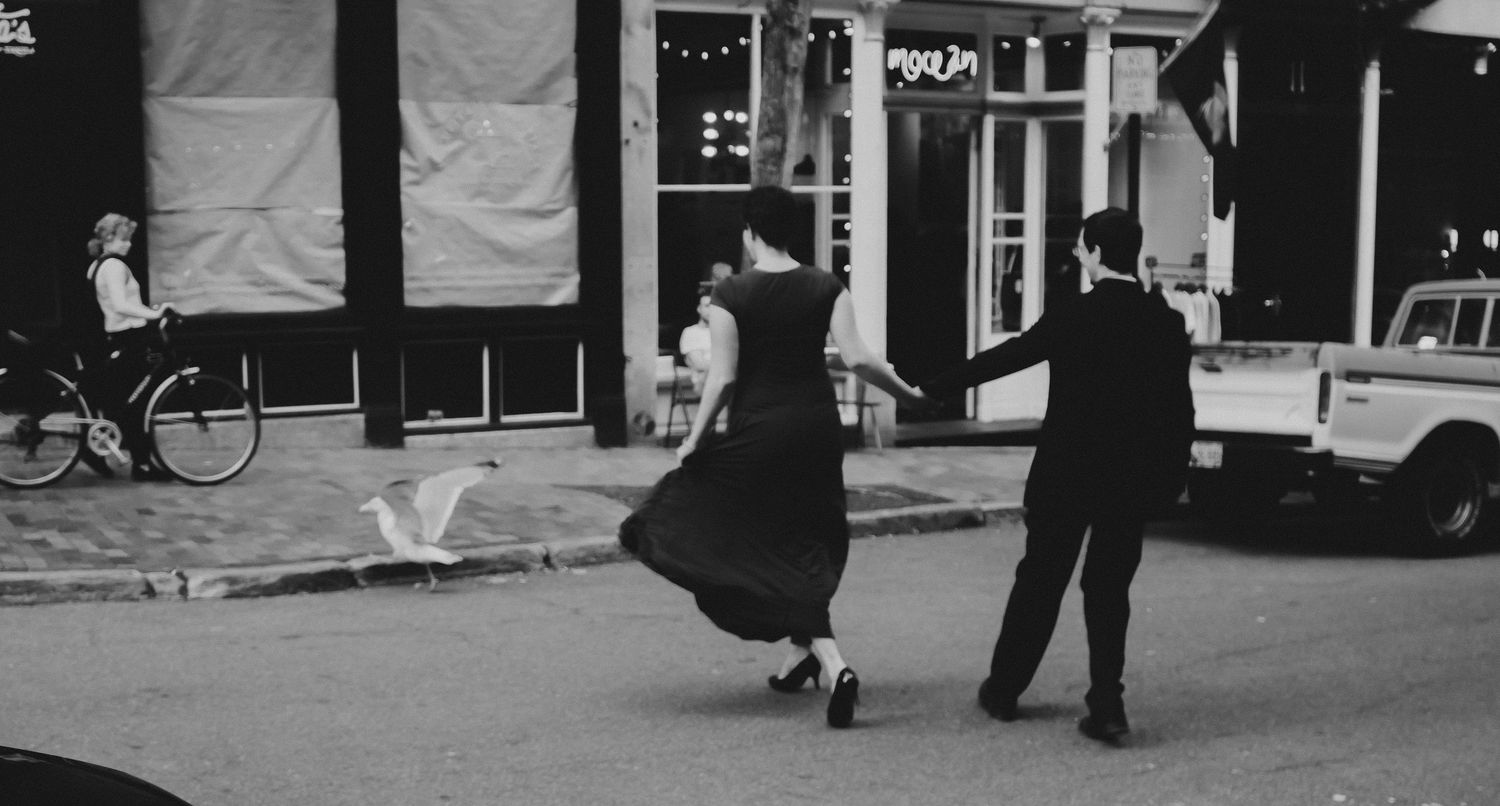 Couple dancing on a city street in black and white, with a bicycle and truck visible in the background.