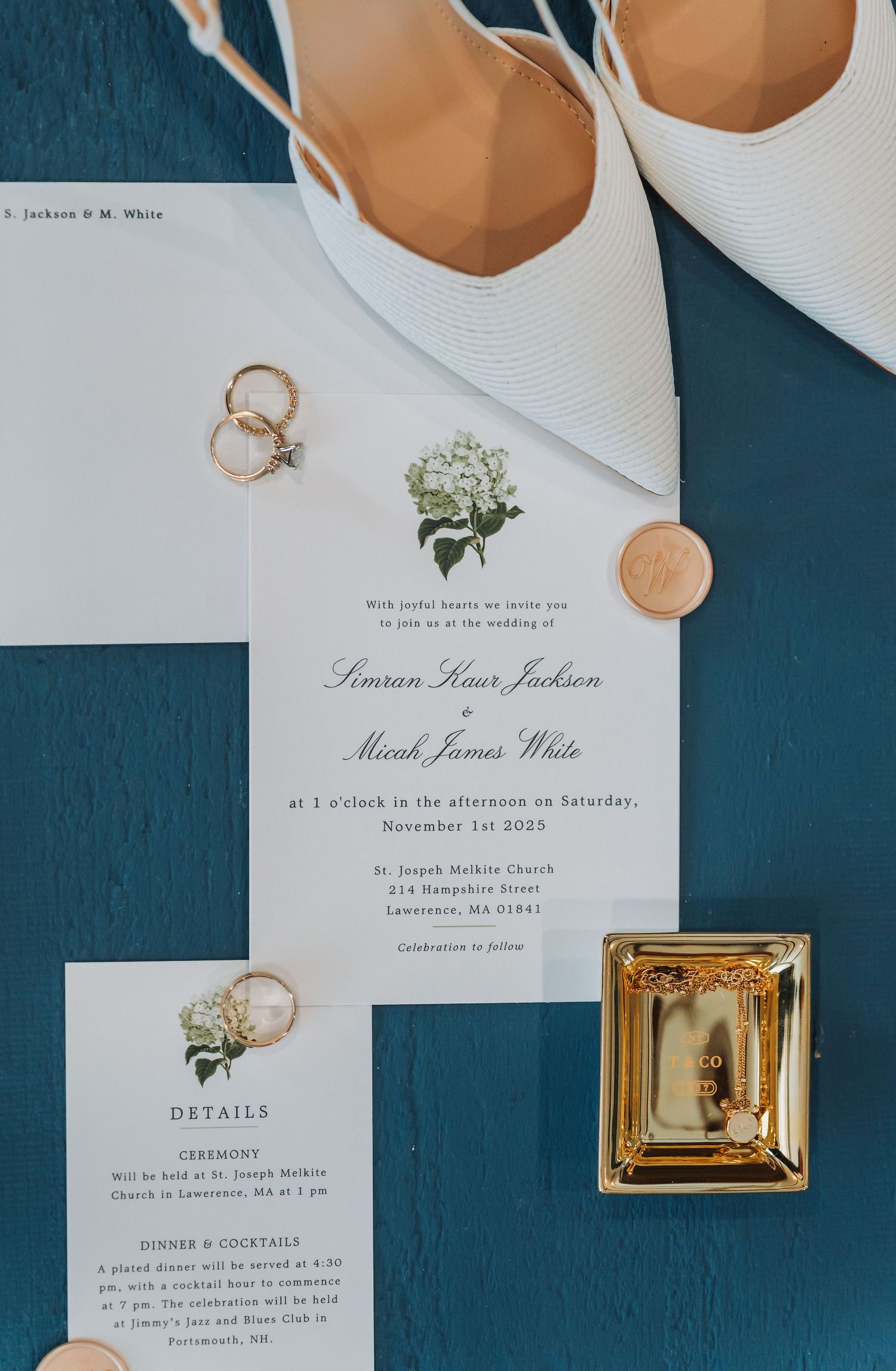 Elegant wedding invitation suite with gold rings, white heels, and floral details on a teal background.