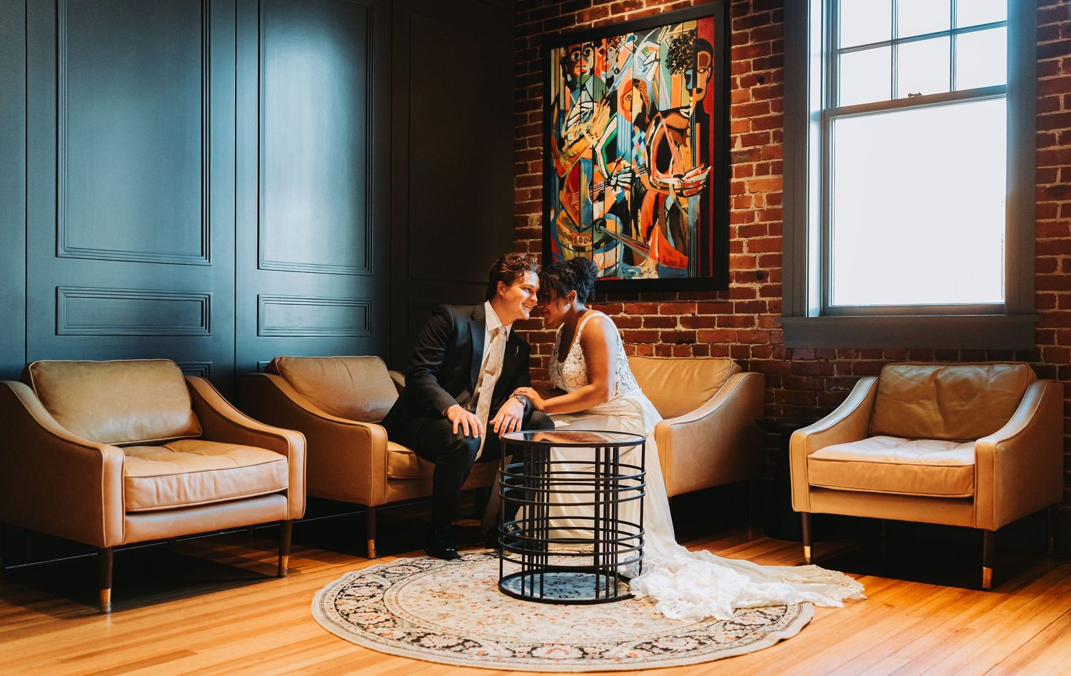 Bride and groom share intimate moment on sofa in stylish venue with exposed brick wall.
