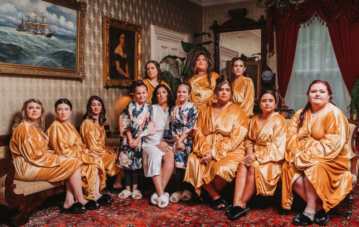 Group of bridesmaids wearing matching gold satin robes posing together in an elegant room.