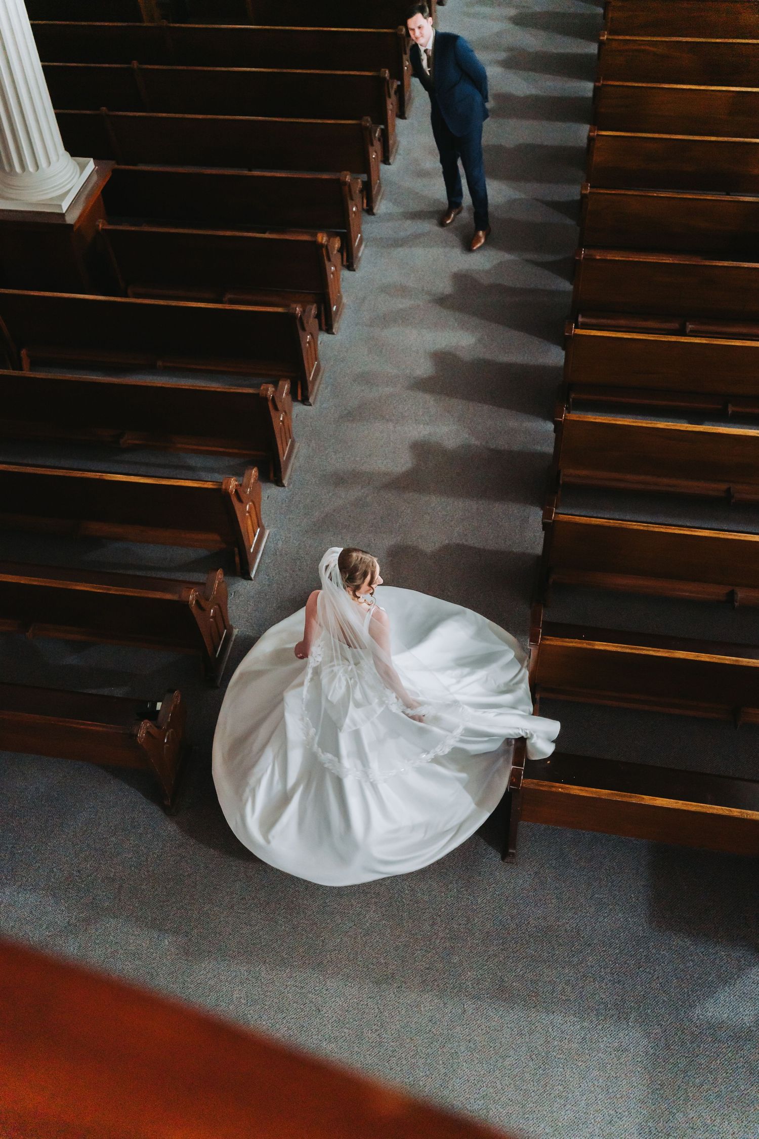 Aerial view of bride in flowing white gown walking down church aisle toward groom.