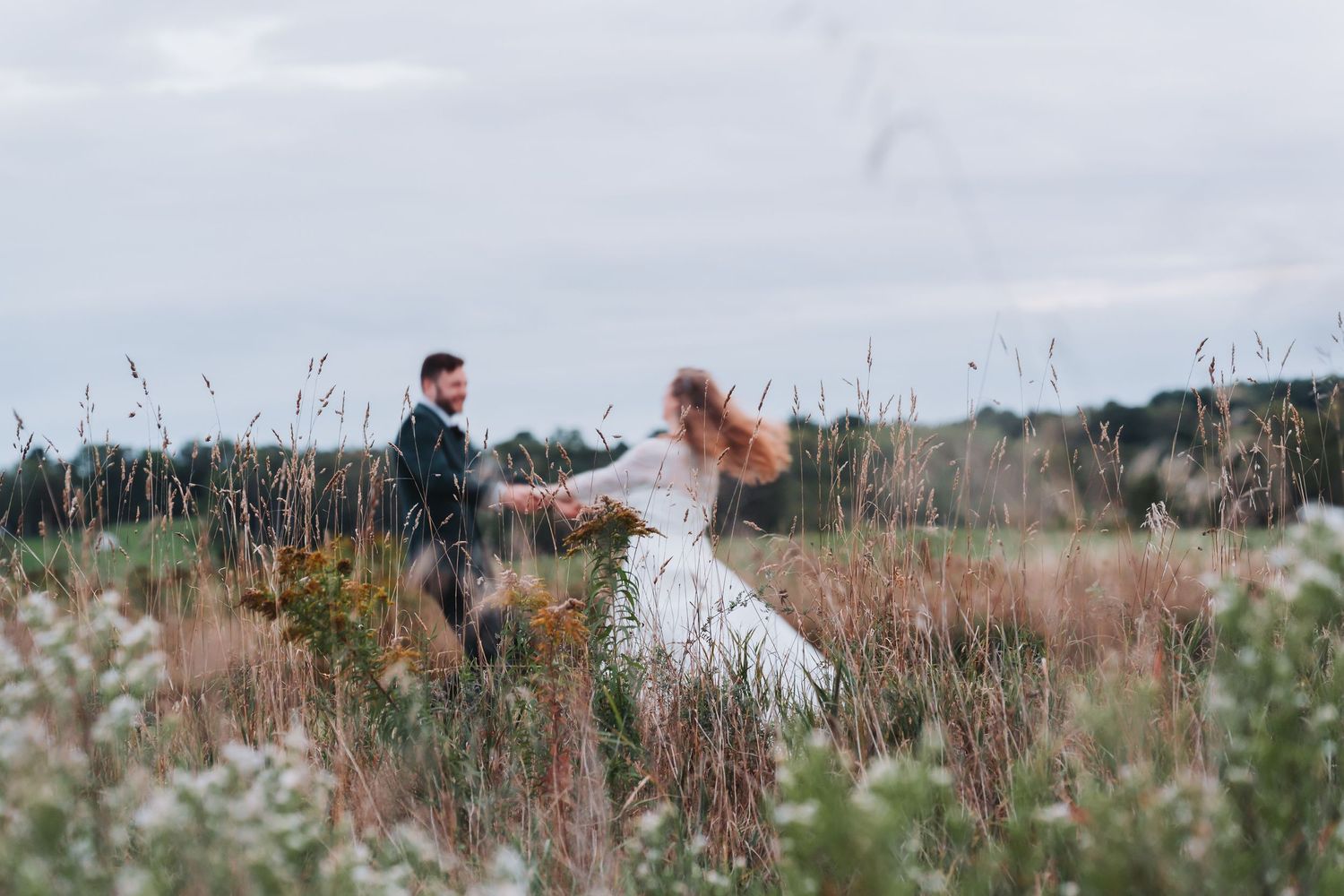 Bride and groom hold hands dancing in a wildflower meadow on their wedding day.