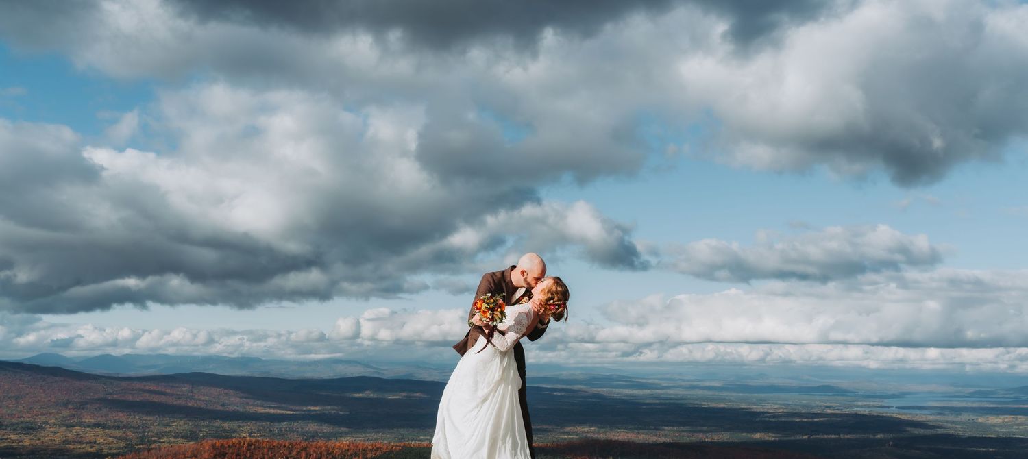 Bride and groom embracing on a scenic hilltop under dramatic cloudy skies.