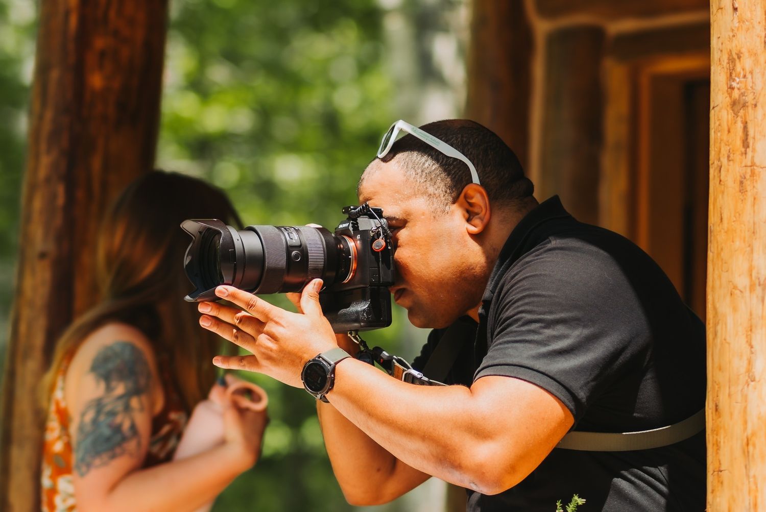 Professional wedding photographer capturing photos with a camera lens in an outdoor wooded setting.