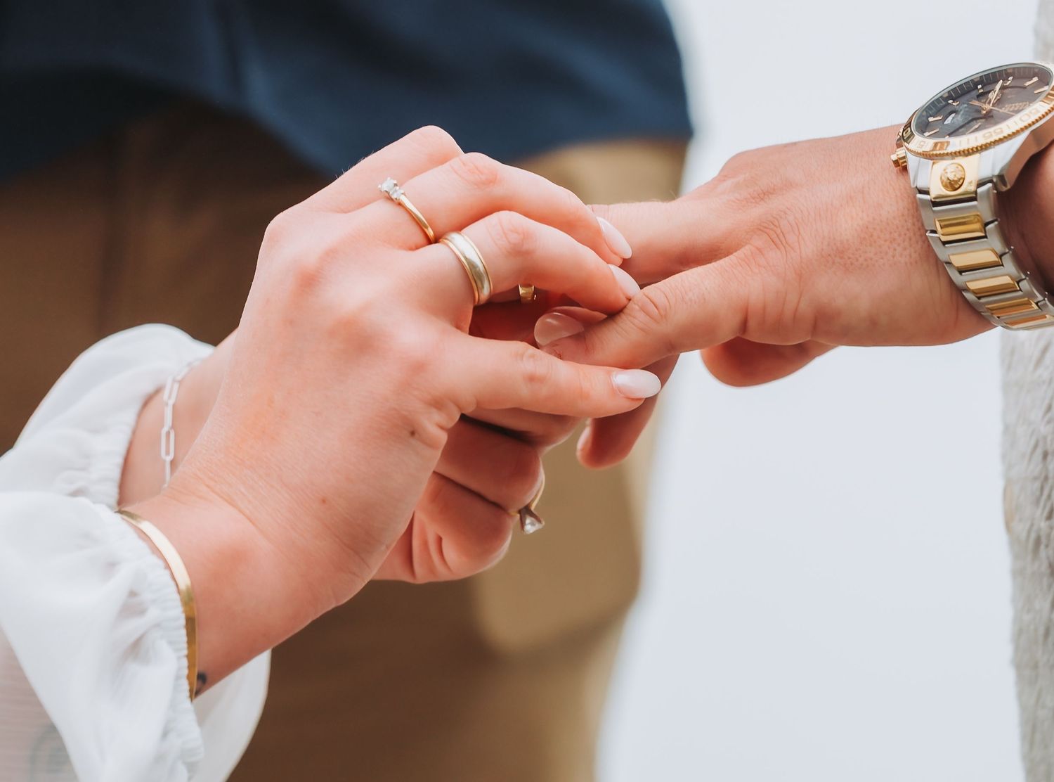 Close-up of newlyweds holding hands showing matching gold wedding bands and a gold watch.