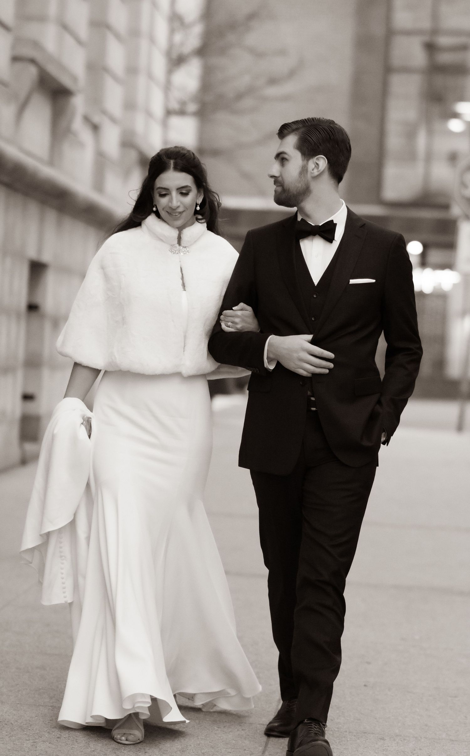 Elegant bride and groom walking arm in arm in black and white portrait.