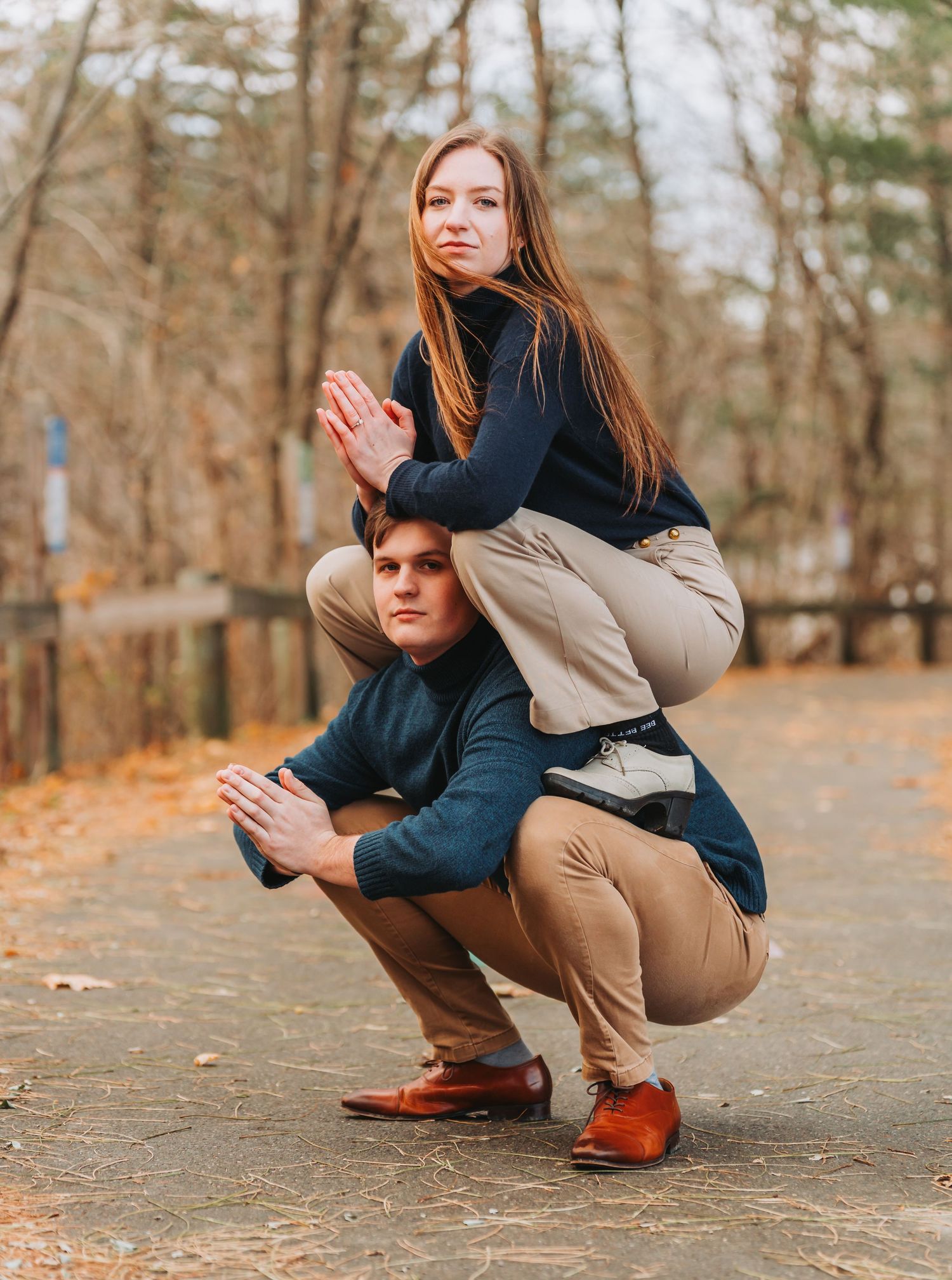 A young couple poses outdoors in matching navy and khaki outfits, with the woman balanced atop the crouching man.