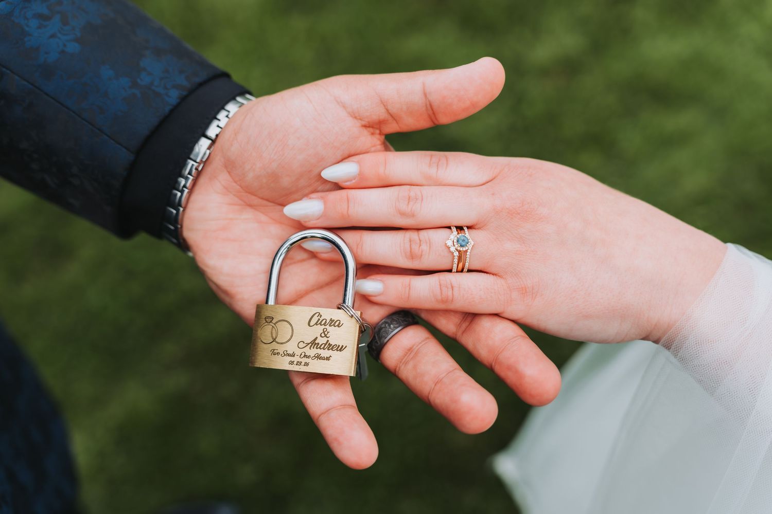 Two hands holding an engraved gold padlock, one wearing a diamond ring, symbolizing a wedding love lock ceremony.
