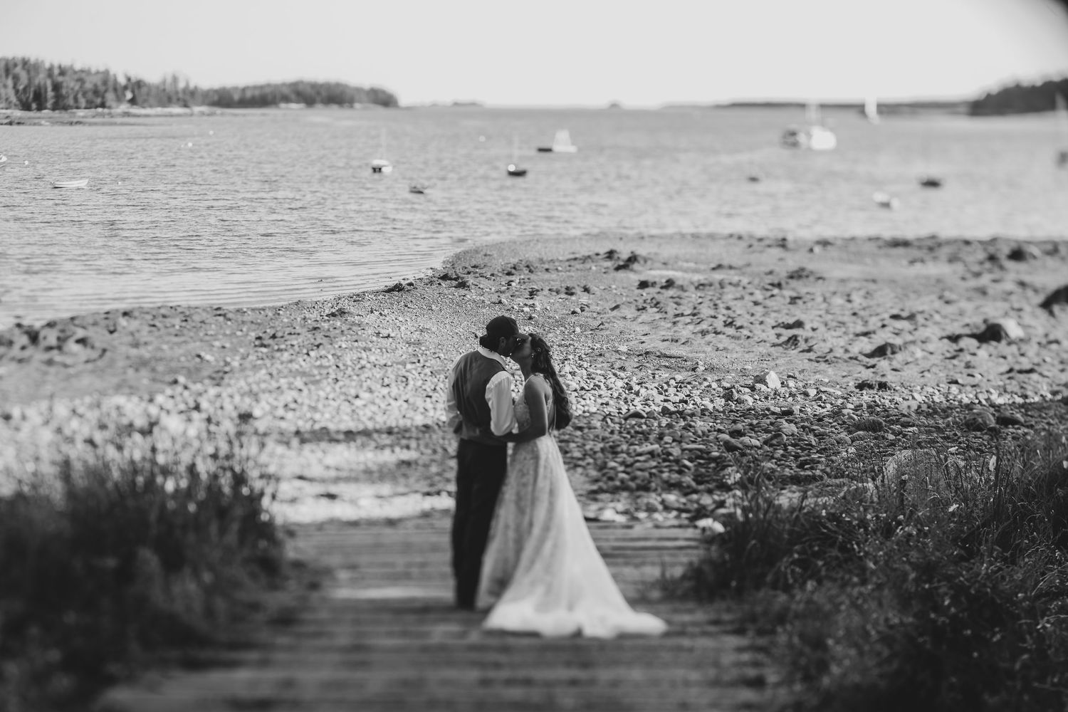 Bride and groom share a romantic kiss on a rocky shoreline in this elegant black and white wedding photo.