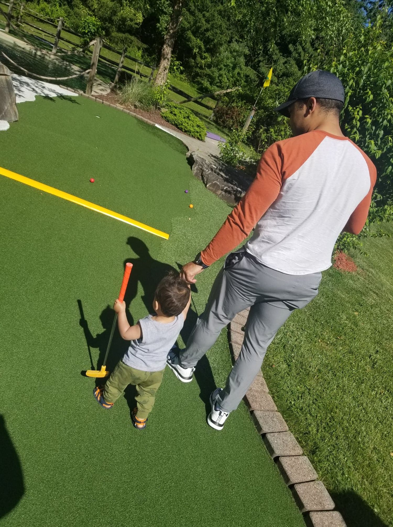 Father and toddler son playing mini golf together on a sunny green course.