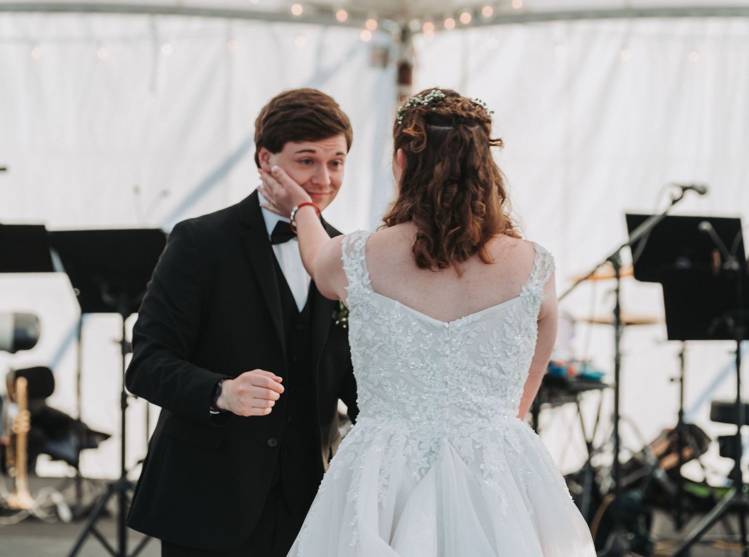 Bride tenderly touches groom's face during emotional first dance at outdoor wedding reception.